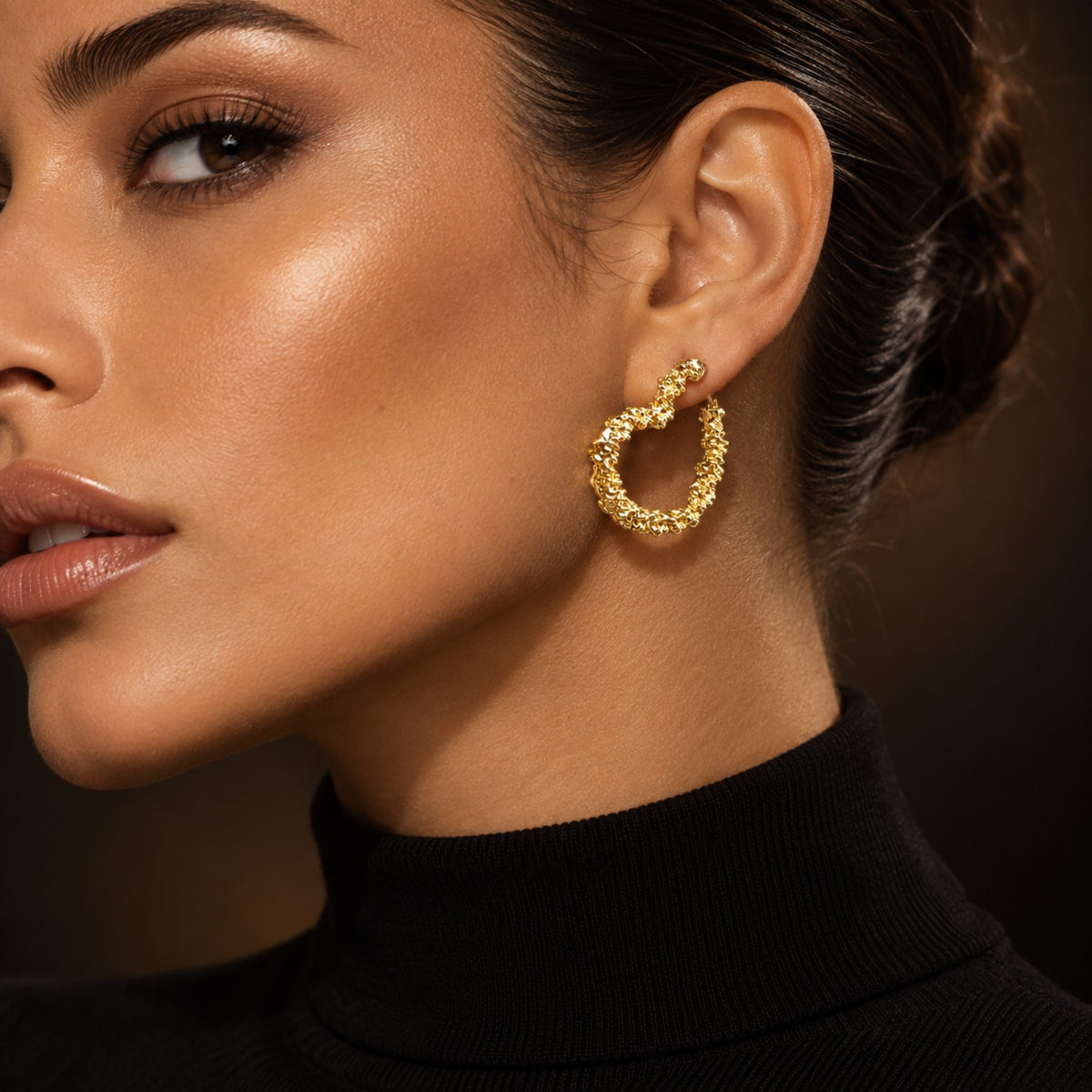 Modelo usando o brinco Argola Aura folheado a ouro, com contorno orgânico e textura em relevo, vendido por par.