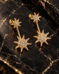 Par de brincos Celeste dois em um folheados a ouro, com duas estrelas cravejadas com zircônias em cada brinco, sobre pedra escura.