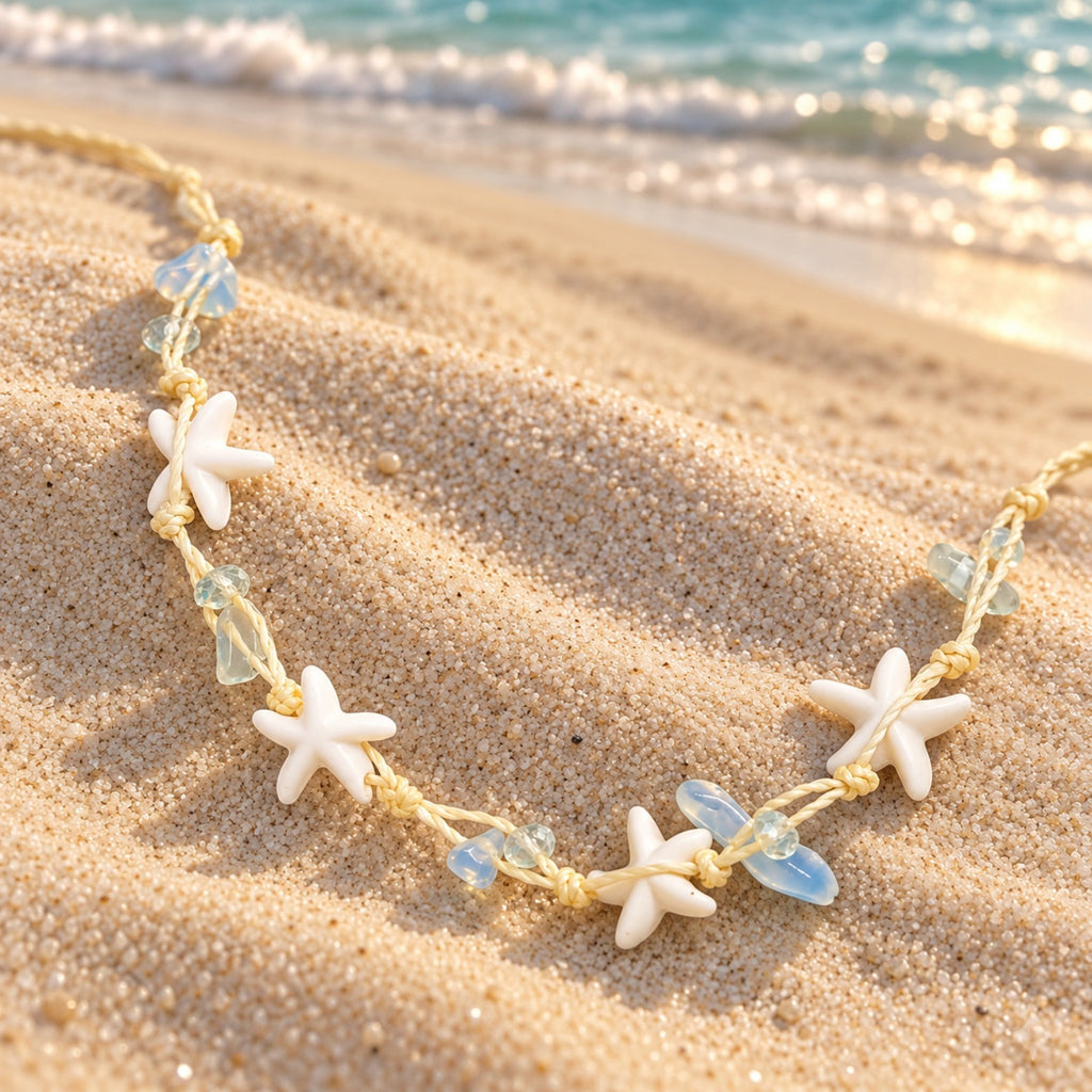 Detalhe do cordão com nós, das estrelas-do-mar e das contas azul-claras e translúcidas do Colar Marina junto à praia.