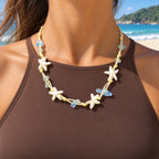 Modelo com blusa marrom usando o Colar Marina Estrelas do Mar Azul em cenário de praia.