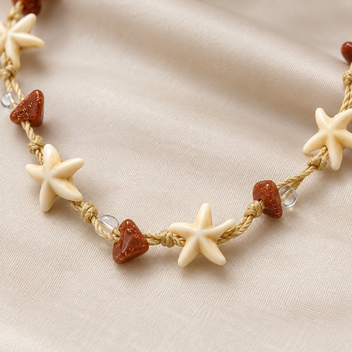 Detalhe das estrelas-do-mar em tom marfim, dos nós do cordão e das contas terracota e transparentes do Colar Nalu.